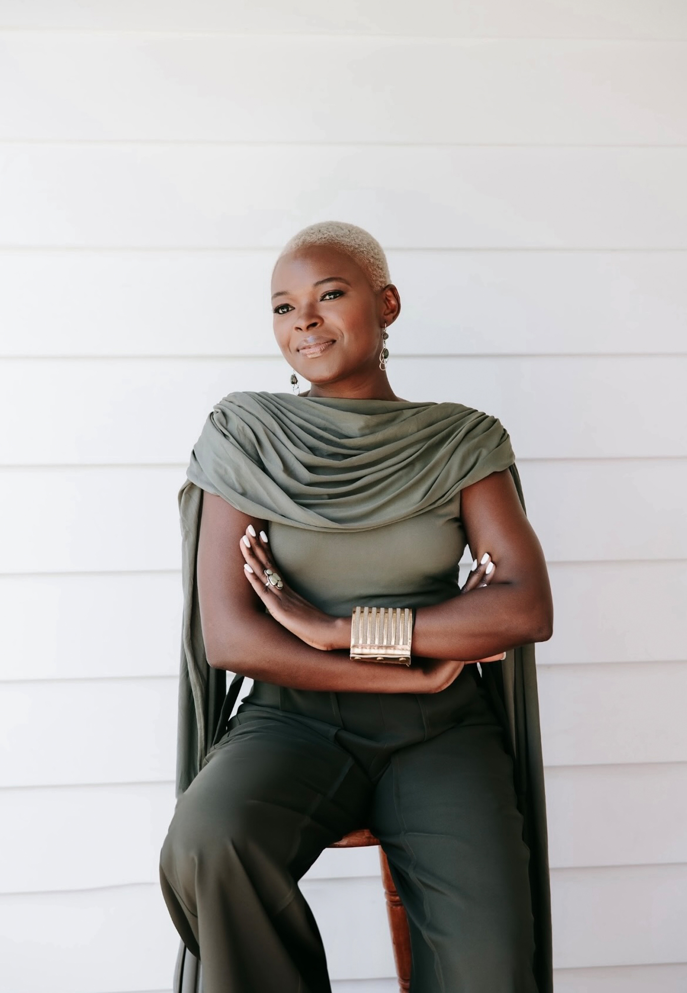 A modern, minimalist bathroom featuring a freestanding white bathtub on a wooden deck, overlooking a lush green garden at sunrise or sunset. Candles and towels add a spa-like ambiance to the tranquil space.