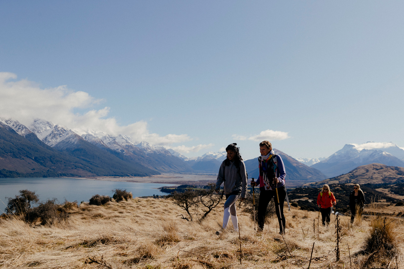 Two hikers trekking through scenic mountain landscape with snow-capped peaks and golden grasslands at Aro Ha