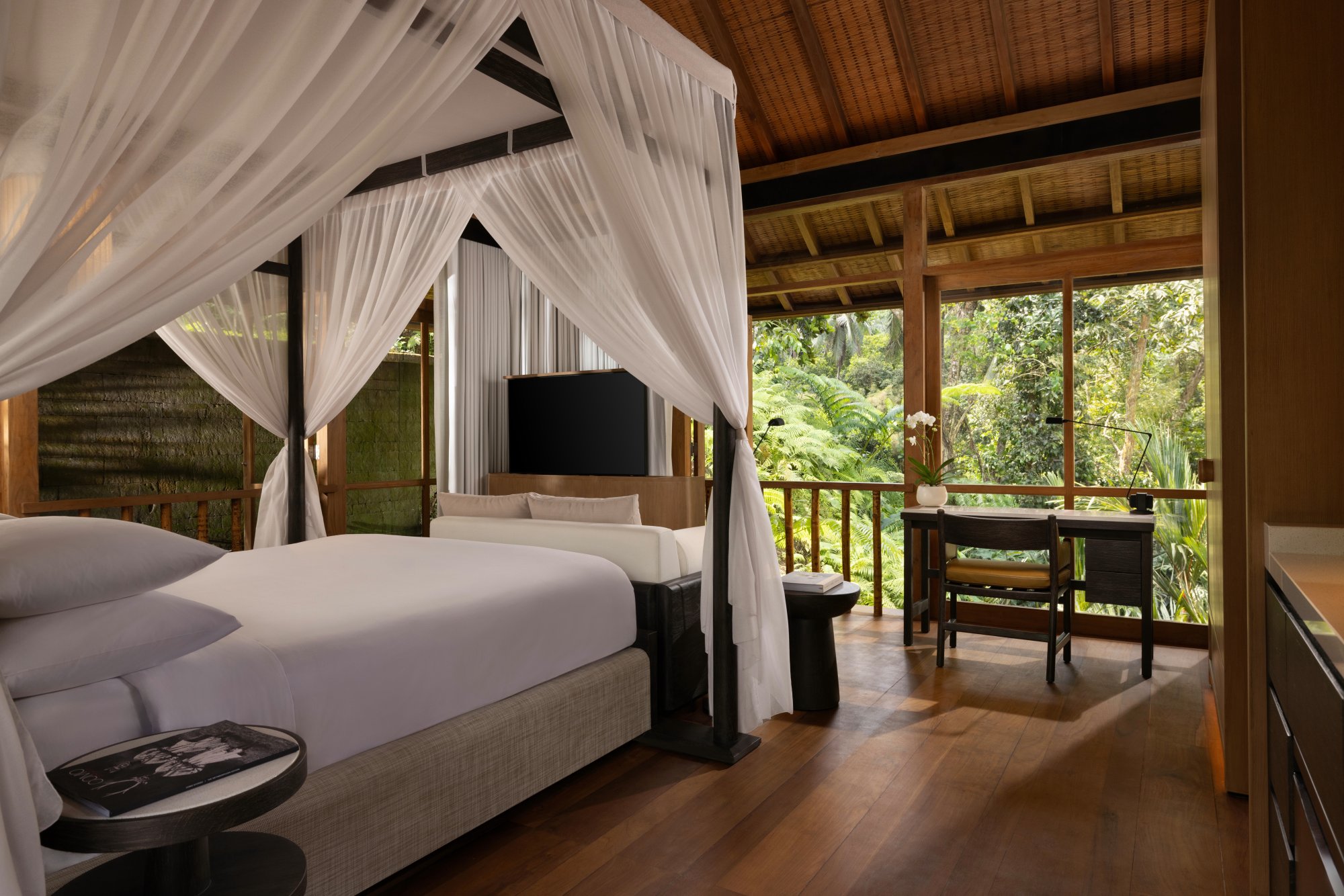 Luxurious Balinese Resort Bedroom with Canopy Bed An elegant tropical bedroom with a four-poster canopy bed, wooden floors, and a large balcony overlooking lush green vegetation. The room features traditional Balinese architectural elements with a modern, minimalist design.