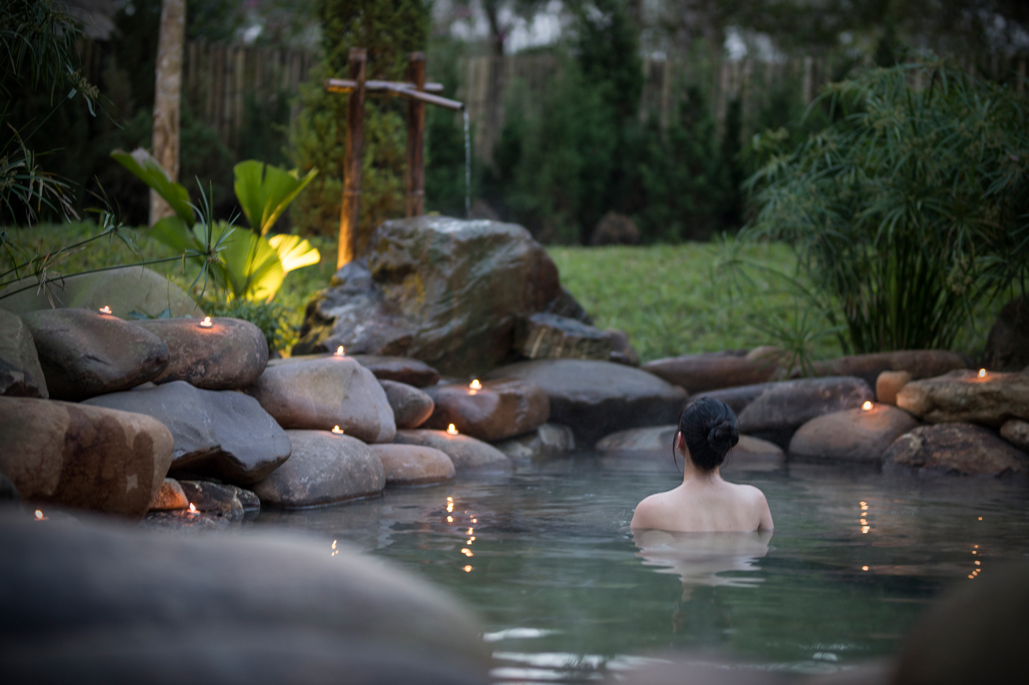 A person floating peacefully in a lush green jungle stream surrounded by ferns and tropical vegetation.